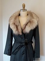 Front view of long black leather coat on mannequin showing fox fur collar and belted waist