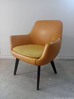 Front and side view showing mustard vinyl tub chair with yellow cushion and black legs on concrete floor.