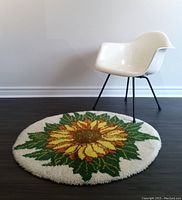Overall view of round sunflower rug beside white chair on dark floor