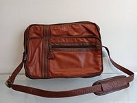 Front view of cognac leather shoulder satchel, showing front zip pocket and vertical strip details, adjustable leather shoulder strap with padded section.