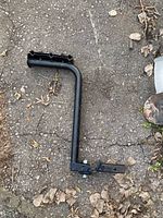 Black metal bike rack arm with mounting bracket and bolt lying on the ground