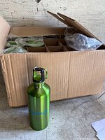 Cardboard box containing 19 green metal water bottles, some bottles wrapped in plastic, one bottle displayed outside the box.