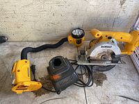 Yellow DeWalt trim saw with visible circular blade, flexible-neck yellow lamp, and black DeWalt battery charger on a dusty surface.