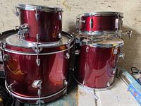 Front view of red drum shells stacked showing floor tom, rack tom, and snare drum with chrome hardware