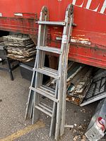 Full view of the folded 16-step aluminum extendable ladder leaning against a red surface outdoors, showing its overall structure and condition.