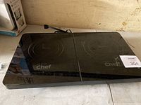 Black glass-top double burner induction stove on a counter with power cord and control panel visible.