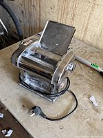 High-end electric pasta maker machine on table with visible power cord and metal casing.