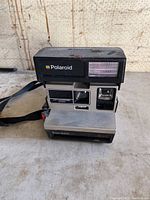 Front angled view of the Polaroid Sun 600 vintage instant camera showing the built-in flash, viewfinder, and logo with strap attached.