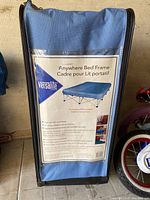 Blue nylon carry bag with label for Versalite Anywhere Bed Frame, stating features and showing graphic of folded bed frame.