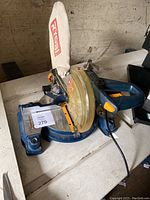 Photo of Ryobi radial arm saw showing setup from the left side, including blue base, blade guard, and connected dust bag.
