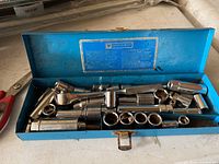 Open blue metal case showing chrome ratchet wrench and multiple sockets inside.