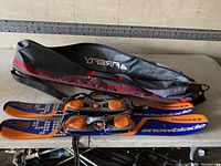 Photo shows pair of short Salomon Snowblade skis with bindings laid on a table and black carrying case.