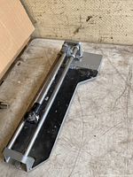 Manual tile cutter placed on a surface showing metal rails and black base, angled view
