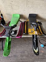 Front view of two vintage GT Snowracers side by side on wooden floor, showing seats, steering wheels, and runners.