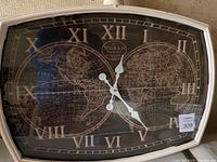 Front view of large wall clock with world map on the face and Roman numerals