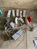 Top view of six Wii remote controllers (one red), four nunchuck attachments (one red), Wii AC power adapter, and AV cable all laid out on a table.