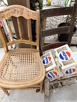 Front view showing antique wooden chair with caned seat, dark wooden rocker frame, and four white Pepsi plastic caddies.