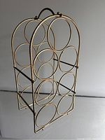 Side angled view of brass wine rack showing seven circular holders arranged in vertical rows with curved arched top handle