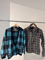 Two clothing items on hangers side-by-side: left is a vintage fleece cardigan with blue and black check pattern, right is a gray and black plaid Bench jacket with zipper.