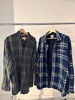 Two flannel plaid L.L. Bean shirts on wooden hangers; one green plaid and one blue plaid fleece-lined tall shirt.
