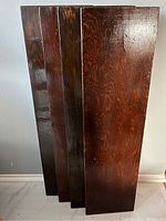 Top down angled view showing four identical wooden shelves stacked leaning against a wall, displaying glossy dark finish and wood grain.
