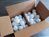 Open large cardboard box with approximately 80 GE 60 watt frosted incandescent bulbs inside, divided by a cardboard partition.