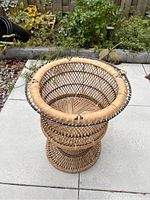 Overview photo showing the wide circular opening and woven construction of the rattan planter placed on patio tiles with garden background.