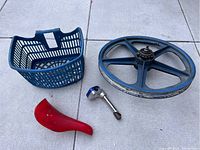 Blue plastic bike basket, red BMX bike seat, and blue mag-style wheel placed on pavement showing all parts in the lot