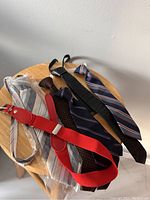 Six vintage kids neckties displayed on a wooden stool, showing variety of colors and patterns including striped, polka dots, solid leather, and bright red with buckle details.