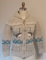 Front view of the sweater on a dress form showing the zipper fully closed, whale motif, collar, and pocket details