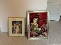 Two framed artwork prints leaning against a wall, one fabric canvas with a child figure, other a portrait of a woman.