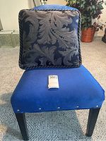 Front view of the blue upholstered chair with decorative cushion on its seat, showing texture and nailhead trim on the seat upholstery.
