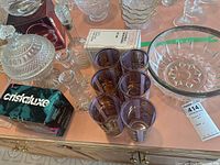 Overview of multiple crystal glassware items including six purple-tinted glasses with gold accents, covered sugar bowl, crystal creamer, candle holders, and other bowls.