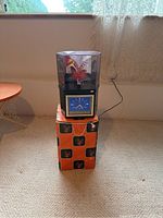 Front view of the flower lamp standing on its box, showing the clear cube with illuminated flower inside and the clock at the base.