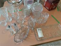 Overall assortment of crystal glassware including glasses, bowls, salt sprinklers, covered candy jar, and serving trays on table