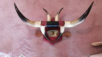 Full frontal view of the mounted horn wall art showing the curved light to dark-tipped horns attached to a red leather backing with black leather wrapping on the top center mount.