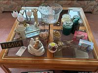 Top-down photo showing entire lot of assorted knick knacks on glass-top table including candles, figurines, glass bowl, and other decorative objects.