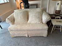 Front view of white loveseat with two matching decorative pillows on a carpeted floor.