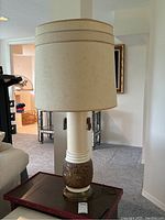 Mid century modern table lamp with cream fabric drum shade and ceramic base, shown in living room.