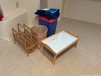 Photo of the entire lot showing the wicker magazine rack, round wicker basket, folding bed tray with white surface, and two plastic storage bins (blue and pink) stacked.