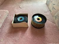 Two containers of 45 RPM vinyl records shown, one white square box and one round decorative tin, records stored inside each.