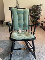 Front view of black wooden rocking chair with green ribbed cushions and button tufting