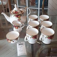 Full tea set including teapot, six coffee mugs, creamer, and sugar bowl on glass table