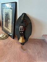 Front view of large mounted Swiss bell on wooden plaque with three smaller wooden cowbells.