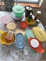 Photo showing boxed assortment of 13 Tupperware containers of varying pastel colors and sizes, including lids, a strainer insert, and pitcher.