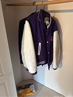 Two West Coast Express purple and white varsity jackets hanging in closet with a folded jacket on the floor.