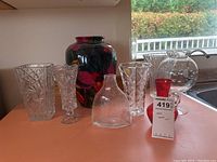 Full view of seven vases showing various sizes and styles including clear cut glass, red floral ceramic, and small red glass vase