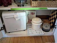 Shelf with bread machine, plastic bucket, yearbook, tray, and coasters