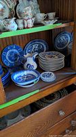 Blue Willow plates and serving pieces, Von Rorfrand cups and plates, Delft coasters displayed on wooden shelf