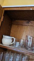 Shelf with white ceramic pitcher with blue rim, clear glass tumblers and smaller stemmed glasses